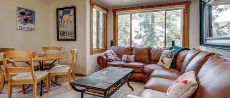 A living room with a brown leather sofa, a wooden dining table with chairs, and a painting on the wall.