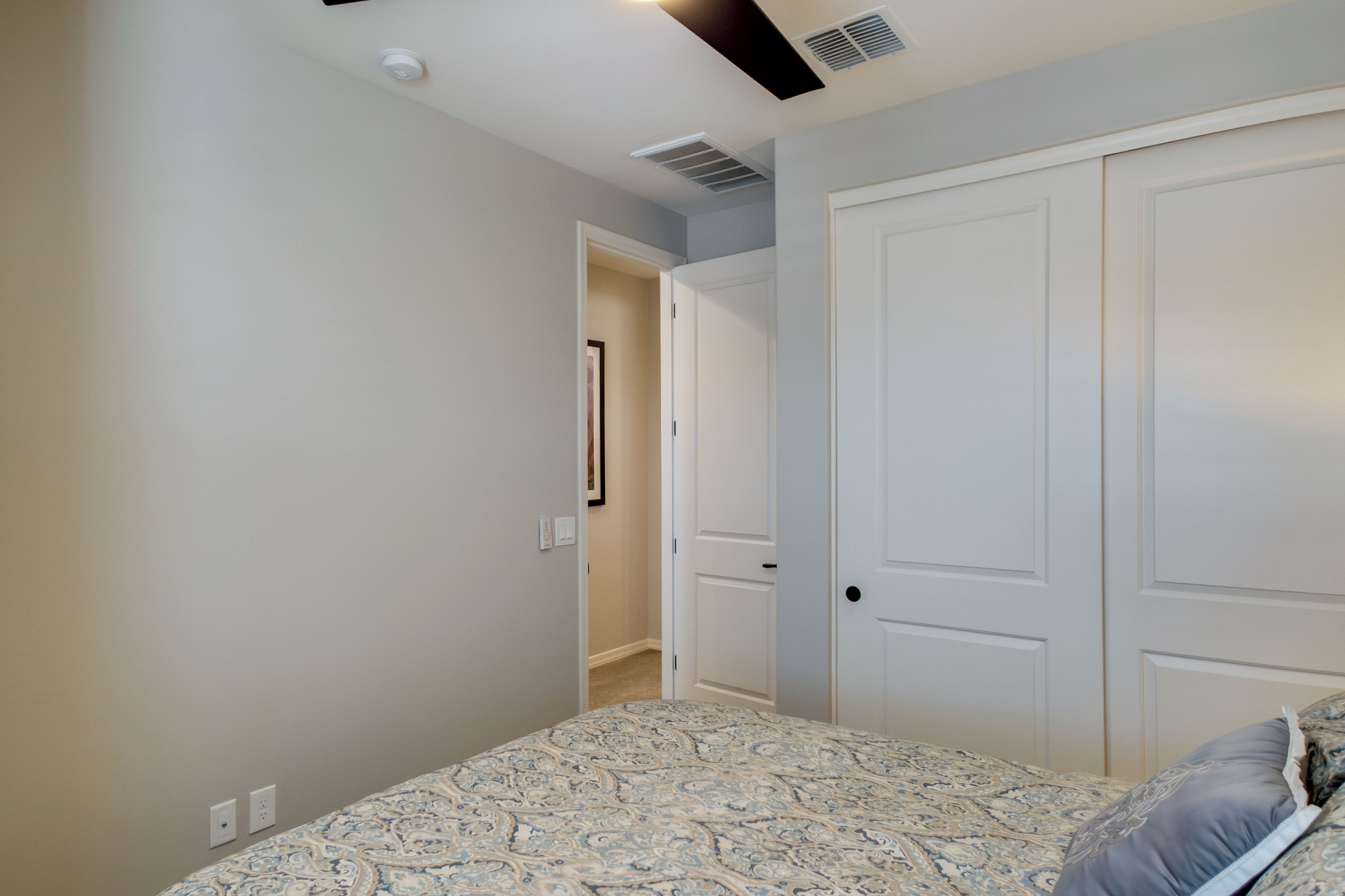 A bedroom with a patterned bedspread, a white door, and a hallway leading to another room.