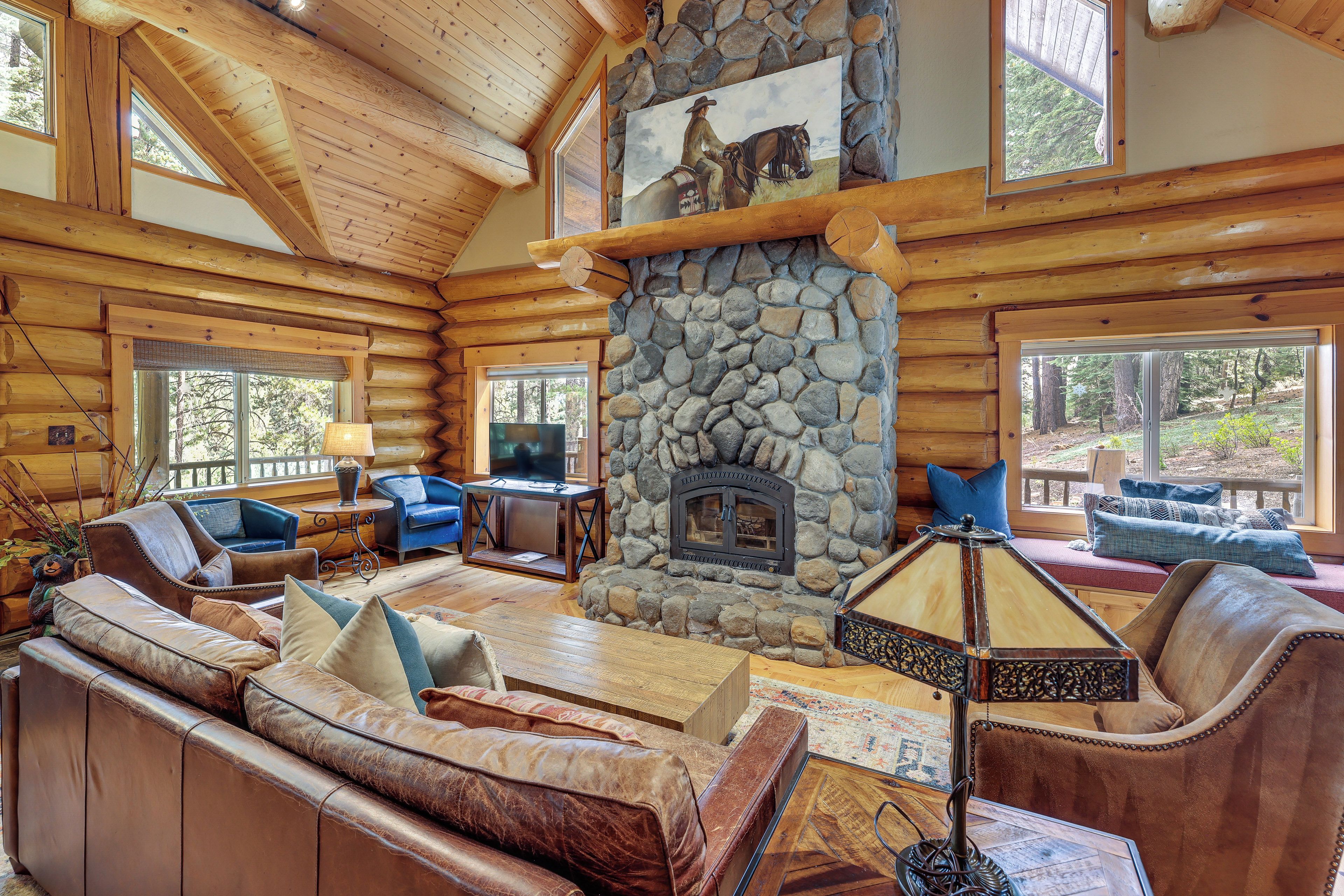 A log cabin interior with a stone fireplace, leather sofas, and a television.