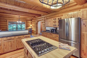 A wooden cabin interior with a kitchen area featuring a stainless steel refrigerator, a gas stove, wooden cabinets, and a chandelier. - All-season Family Cabin w/ Forest Views in Truckee (Truckee)