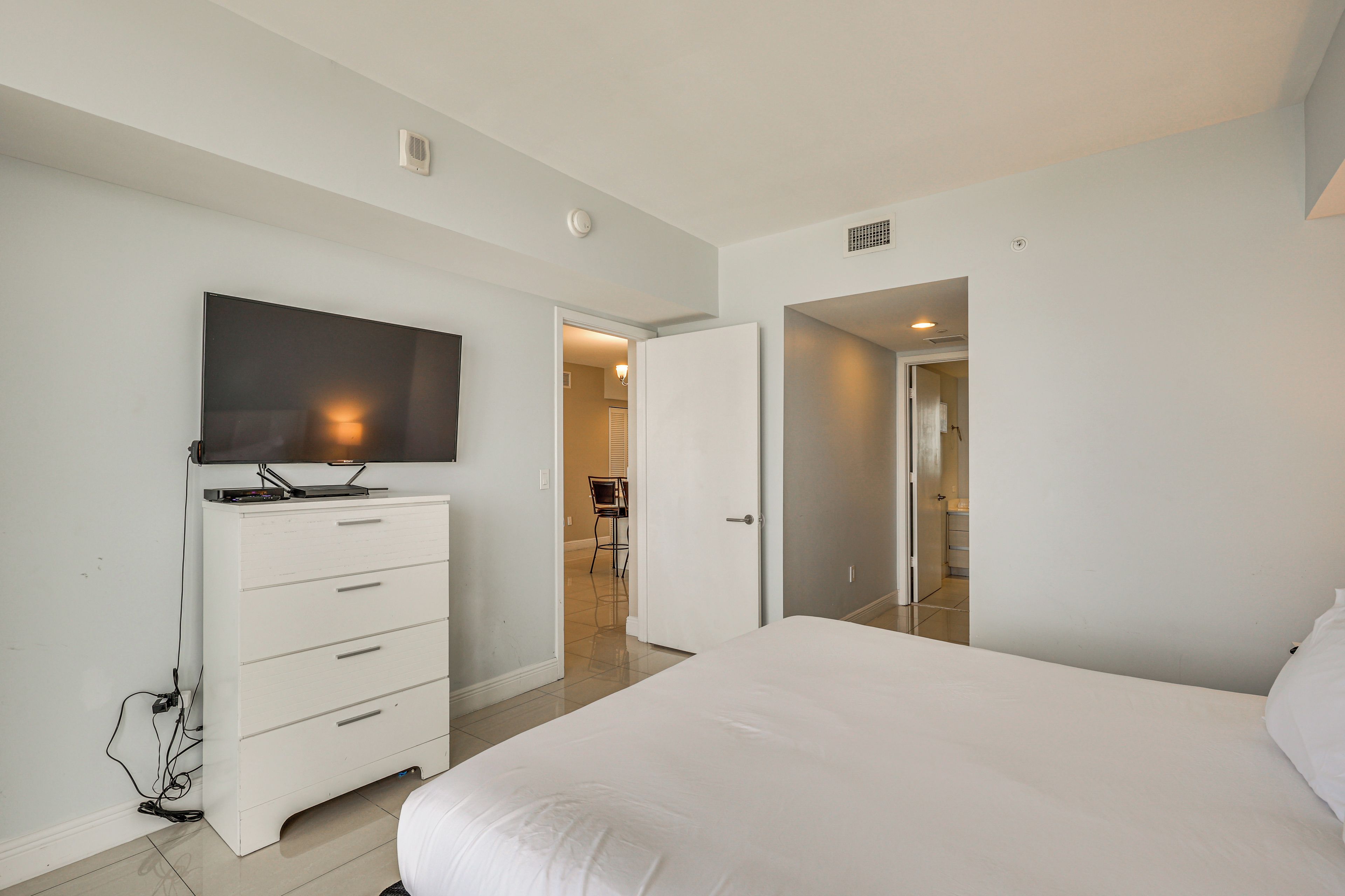 Un dormitorio con cama, cómoda, televisor y puerta que da a otra habitación.