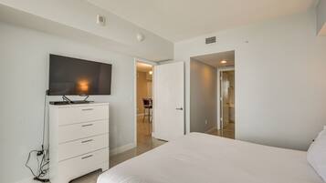 Un dormitorio con cama, cómoda, televisor y puerta que da a otra habitación.