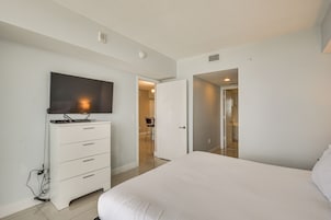 Quarto com cama, cômoda, televisão e porta que dá para outro ambiente.