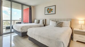 Habitación de hotel con dos camas, un balcón, vistas a la ciudad y una obra de arte enmarcada en la pared.