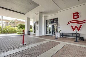 Entrada de um prédio com um grande logotipo, um portão na entrada e um banco.