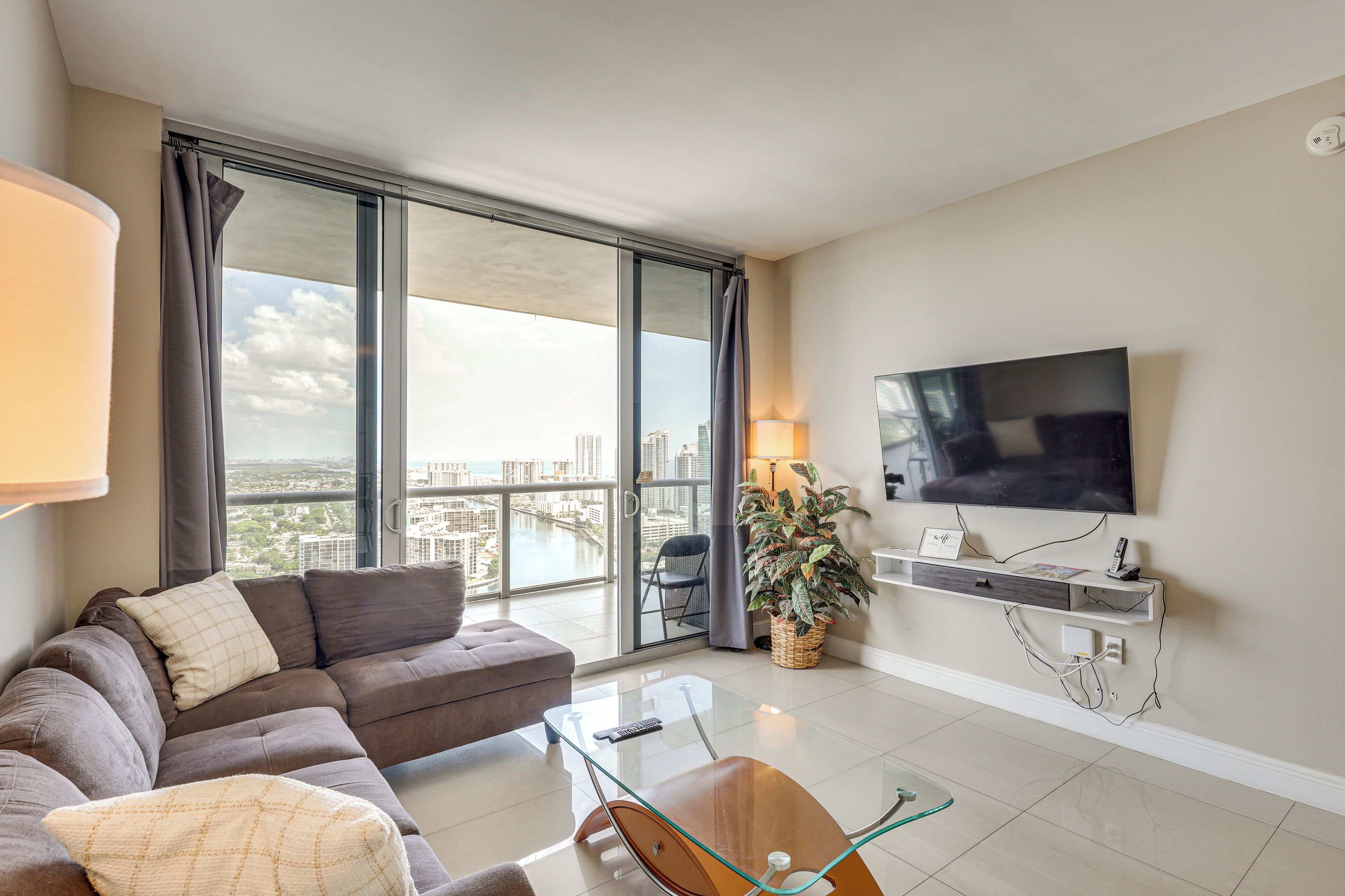 A modern living room with a sofa, a glass coffee table, a TV, and a view of the city.