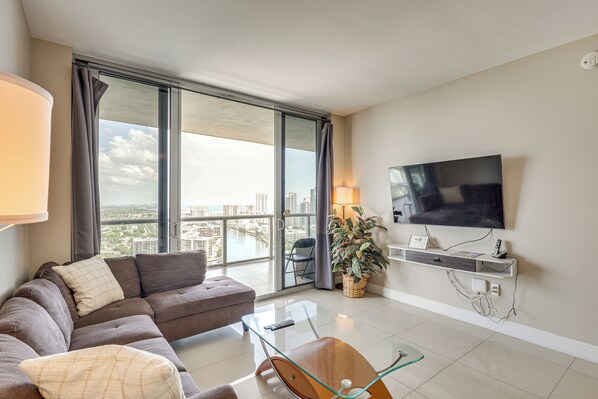 Una sala de estar moderna con un sofá, una mesa de centro de vidrio, un televisor y vistas de la ciudad.