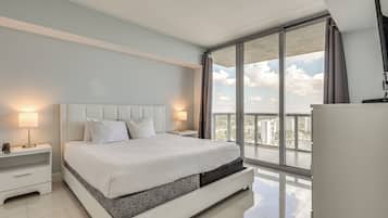 Une chambre d’hôtel moderne avec un grand lit, une table de chevet, une lampe et une vue sur la ville grâce à une grande fenêtre.