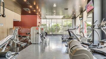A gym with various exercise equipment, a mirrored wall, and a view of greenery outside.