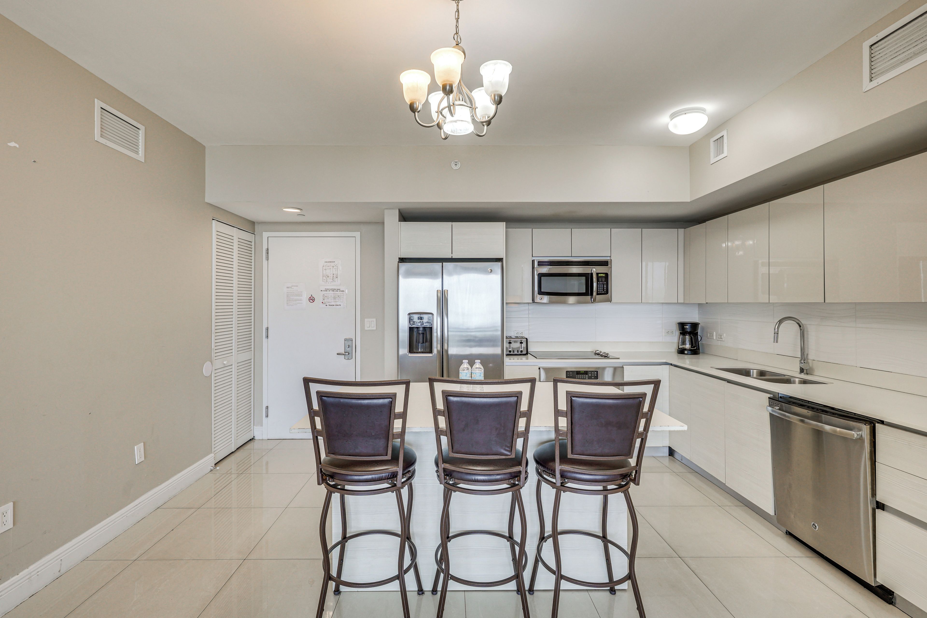 A modern kitchen with stainless steel appliances, a dining area with four chairs, and a chandelier.