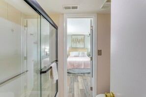 A hotel room with a glass shower enclosure, a bed with a pink bedspread, and a light-colored floor. - Condo w/ Pool & Hot Tub, Short Walk to Beach (Myrtle Beach)