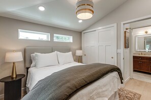 Een slaapkamer met een bed, nachtlampen, een raam en een deur naar een badkamer.
