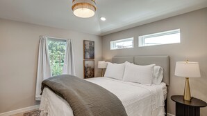Ein Schlafzimmer mit Bett, Nachttischlampe, Fenster und Deckenleuchte.