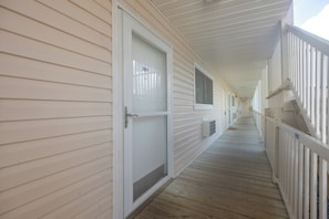A corridor with a wooden deck, white railings, and doors with windows. - Community Pool & Private Patio! N Myrtle Beach Gem (North Myrtle Beach)