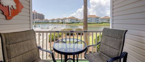 A balcony with two chairs and a table, overlooking a body of water and buildings.
