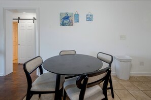 A dining area with a round table and four chairs, a white trash bin, and two wall-mounted decorative items. - Community Pool & Private Patio! N Myrtle Beach Gem (North Myrtle Beach)