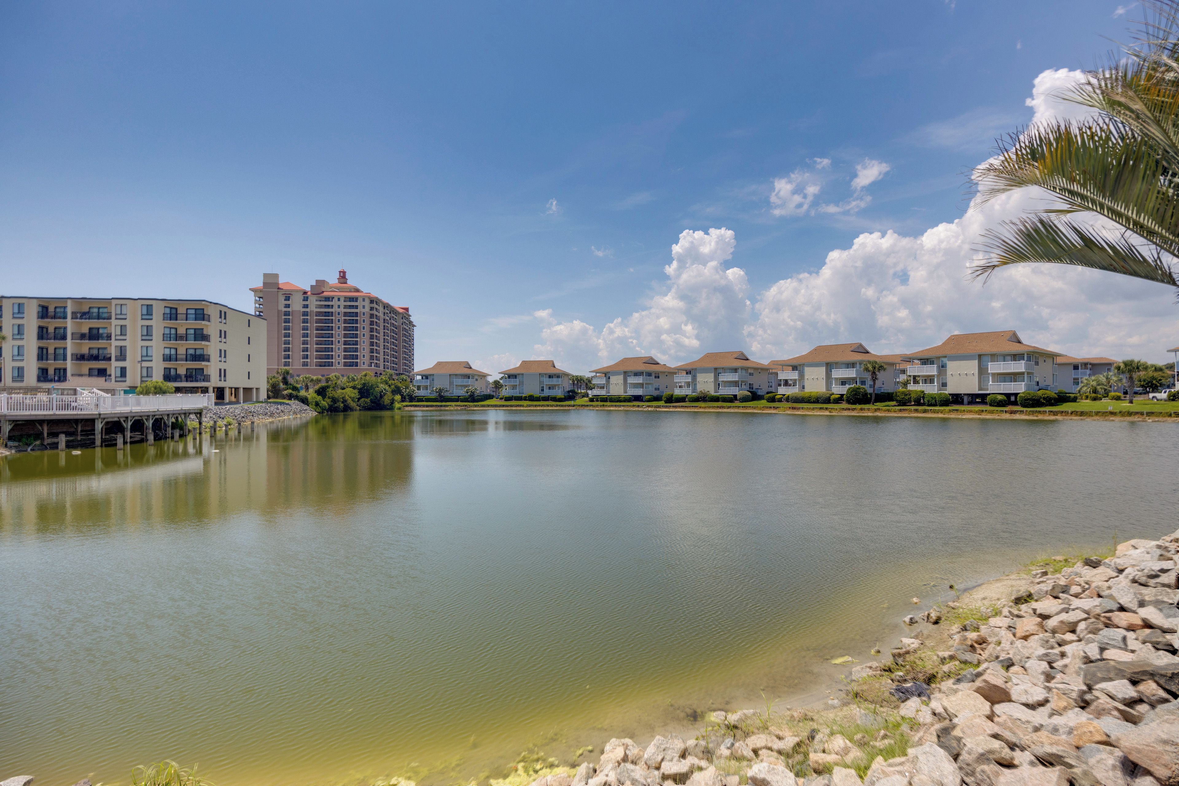 A waterfront property with a calm lake, a bridge, and a row of multi-story buildings with balconies.