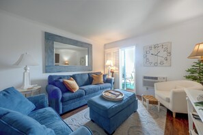 A living room with a blue sofa set, a coffee table, a white armchair, a mirror, and a wall clock. - Community Pool & Private Patio! N Myrtle Beach Gem (North Myrtle Beach)