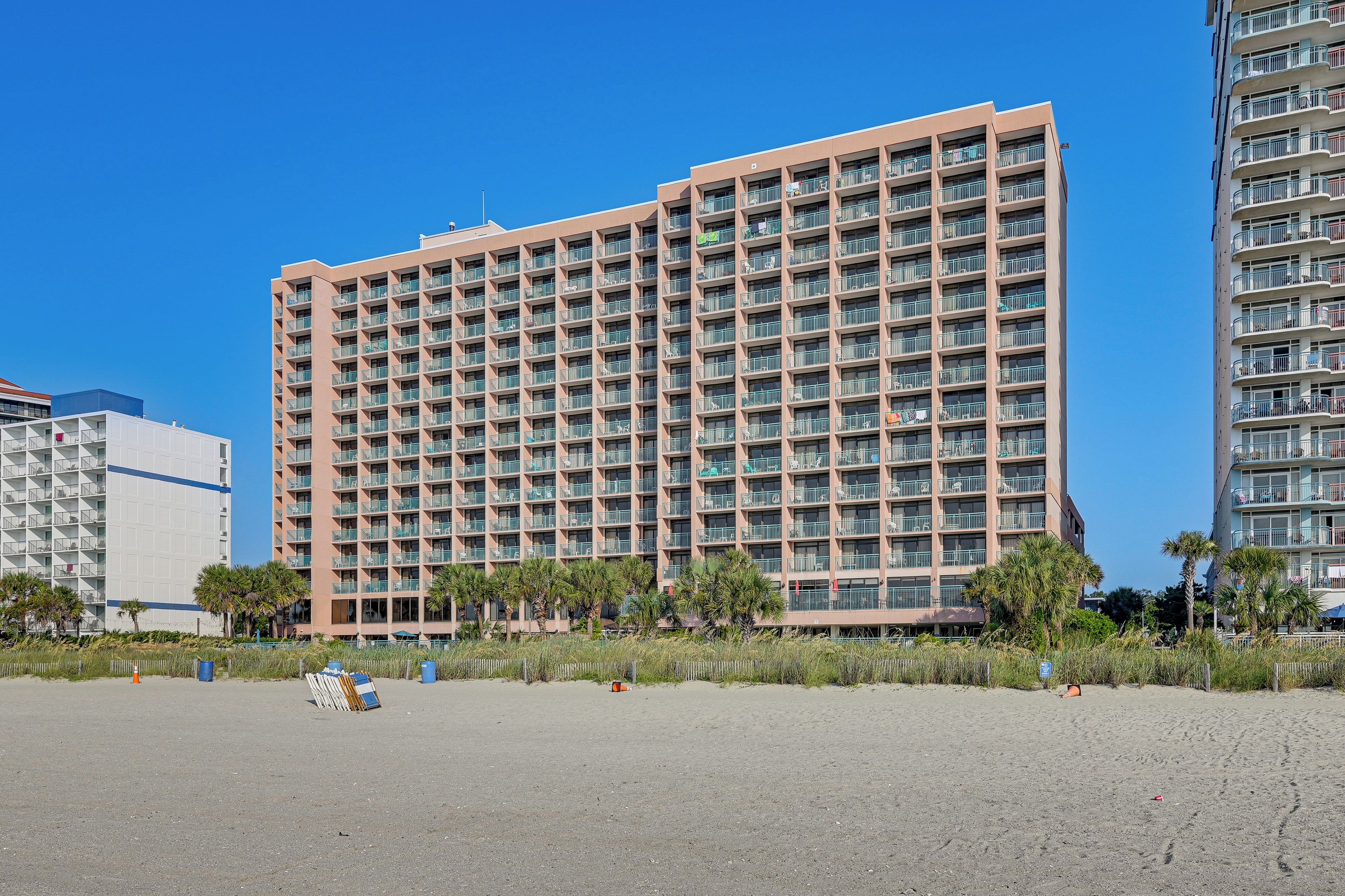 Un hotel de varios pisos con balcones, estacionamiento y palmeras.