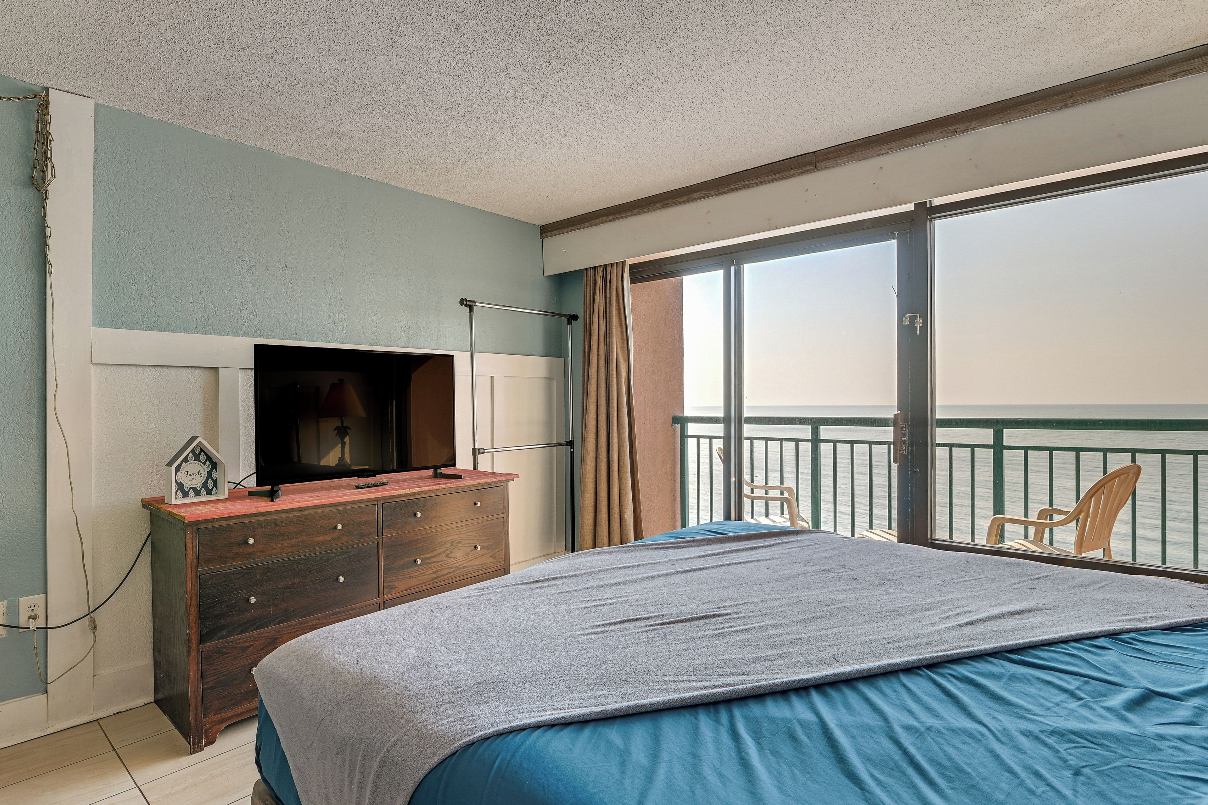 Ein Schlafzimmer mit Bett, Kommode, Fernseher und Meerblick vom Balkon.