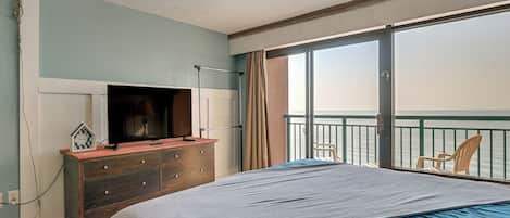 Un dormitorio con cama, cómoda, televisor y vista al mar desde un balcón.