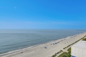 A beach with a long stretch of sand, a pier in the distance, and a clear blue sky. - 14th-floor Ocean View + Pools! Myrtle Beach Haven (Myrtle Beach)