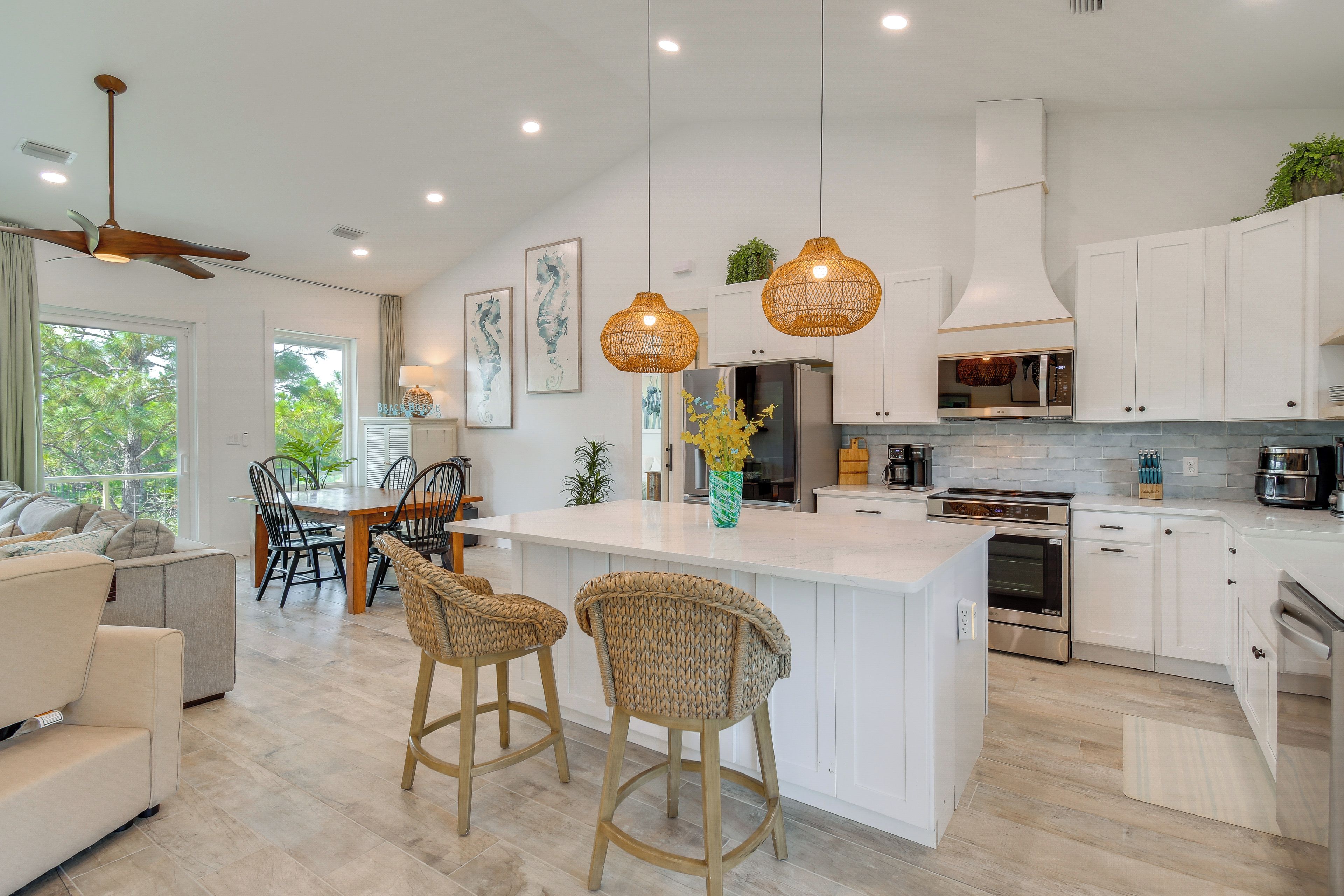A modern kitchen with white cabinetry, a central island with bar stools, pendant lighting, and a dining area with a table and chairs.