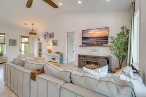 Una sala de estar moderna con un sofá modular, una chimenea y una pantalla grande mostrando un atardecer.