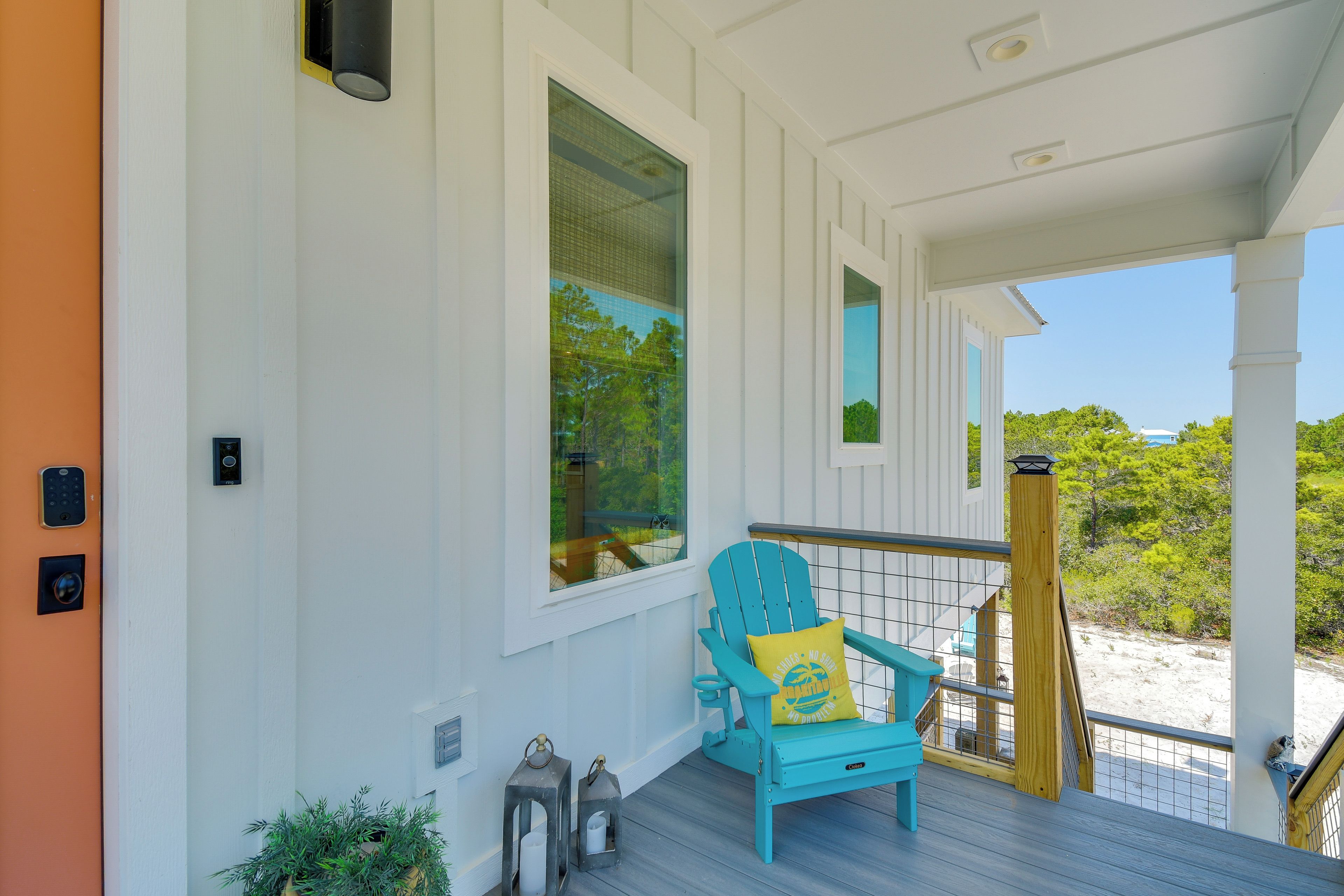 A porch with a blue Adirondack chair, a small railing, and a view of the beach.