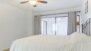 Un dormitorio con una cama grande, un ventilador de techo y vistas al exterior a través de una puerta corrediza.