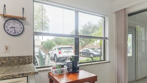 Una cocina con ventana, un reloj y una mesa con cafetera.