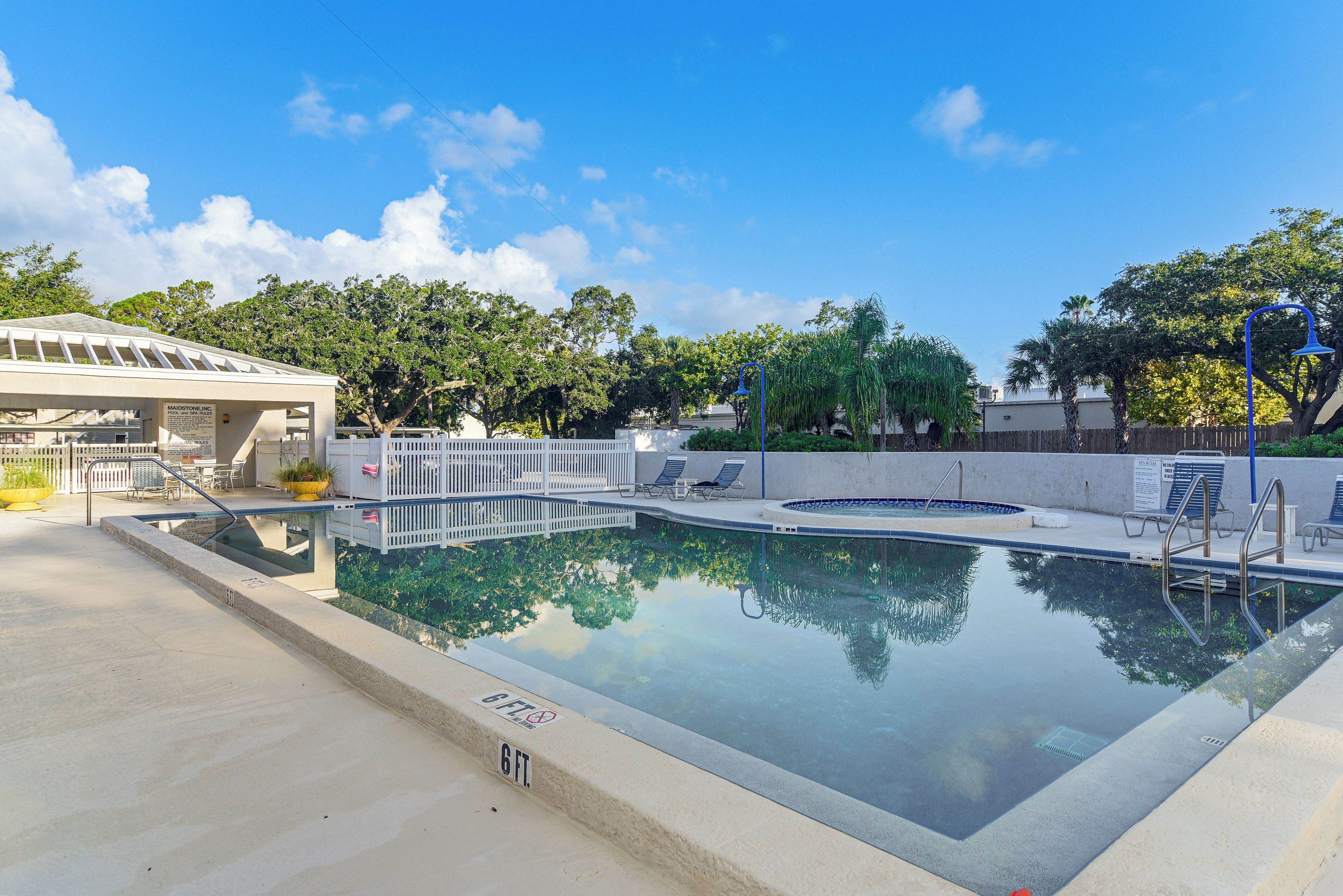 Une piscine avec une terrasse blanche, des chaises longues et un espace abrité agrémenté d’un panneau.
