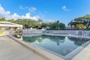 Una piscina con un deck blanco, sillas de descanso y una zona cubierta con un letrero.