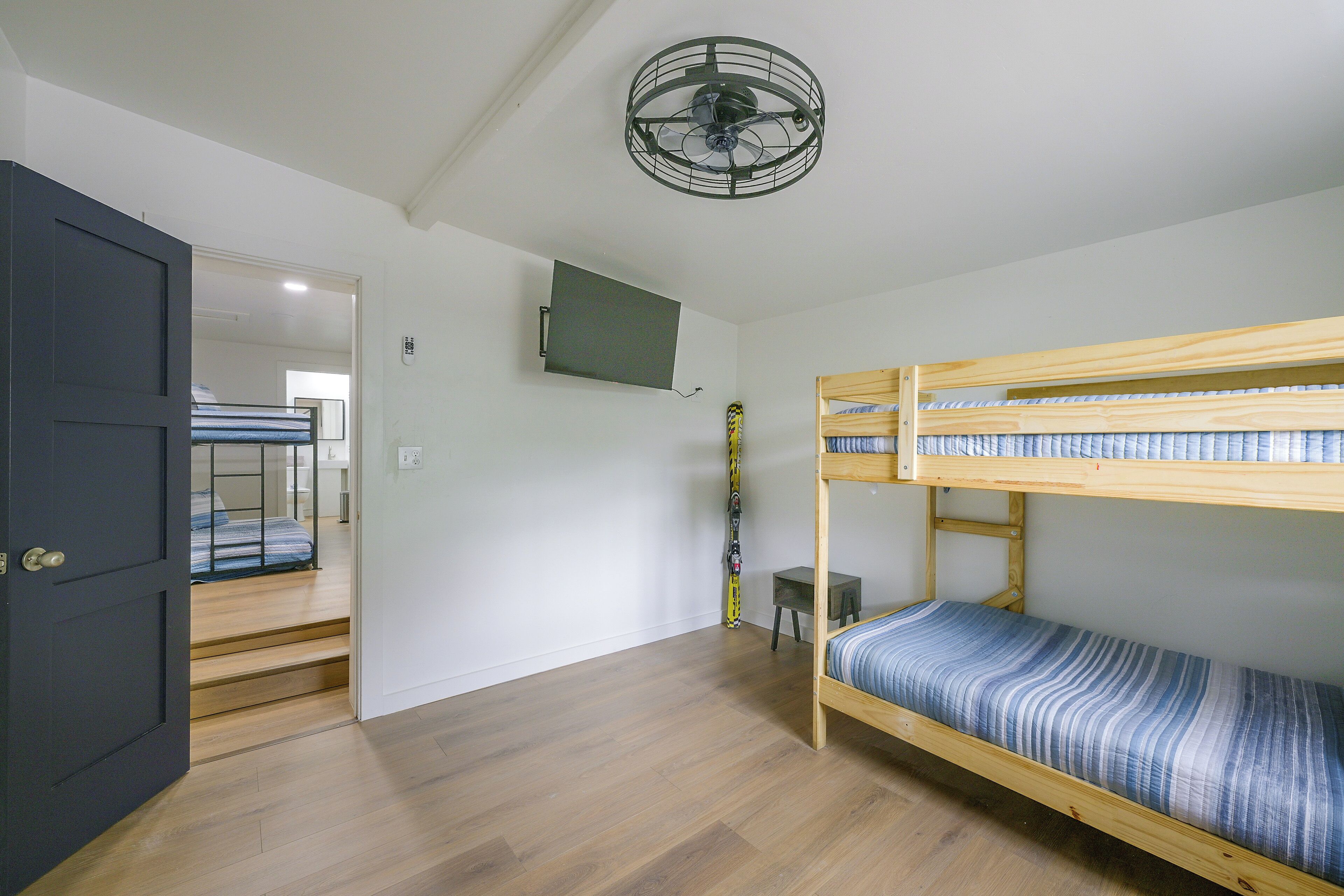 Ein Zimmer mit Etagenbett, einer Tür, einem Deckenventilator, einem Fernseher und einem Snowboard.