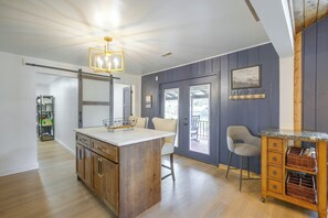 A kitchen with a central island, wooden cabinets, a hanging light fixture, and a view through a door to an outdoor deck.