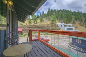 A wooden deck with a table and chairs, overlooking a construction site and a hilly landscape with trees.