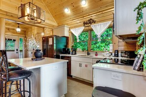 Eine moderne Küche mit einer zentralen Kochinsel, Barhocker, einem Kühlschrank und einem Fenster mit Vorhängen.
