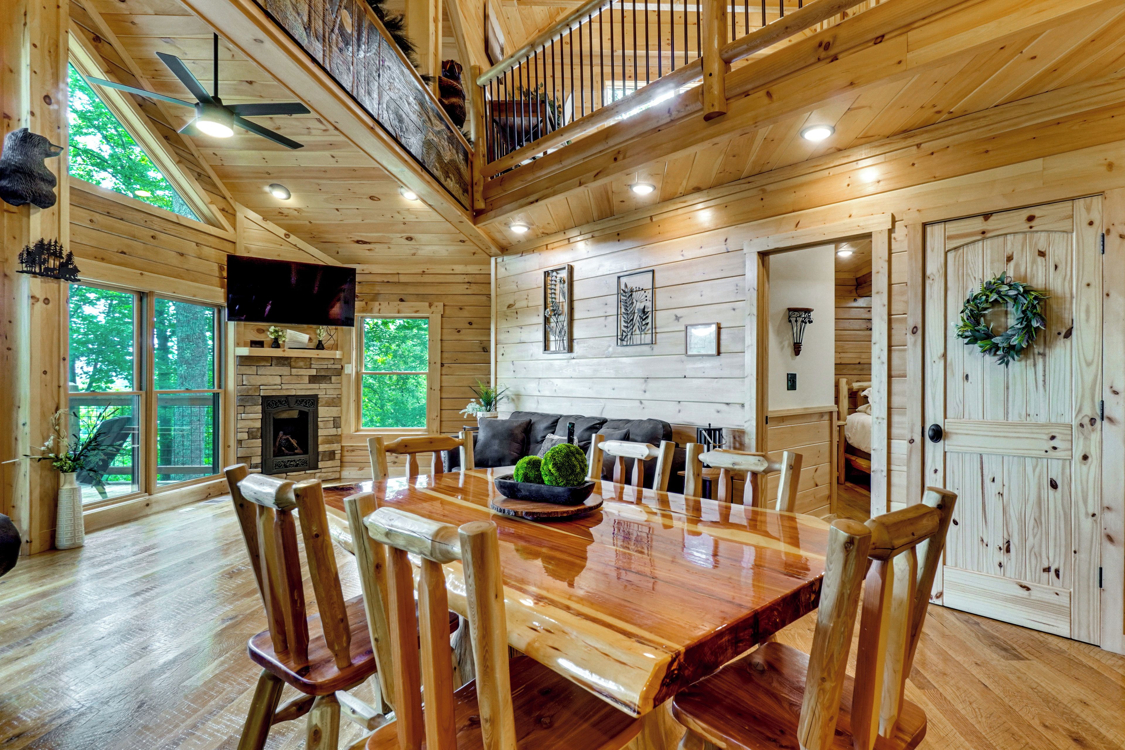 A wooden cabin interior with a dining area, a fireplace, and a staircase.
