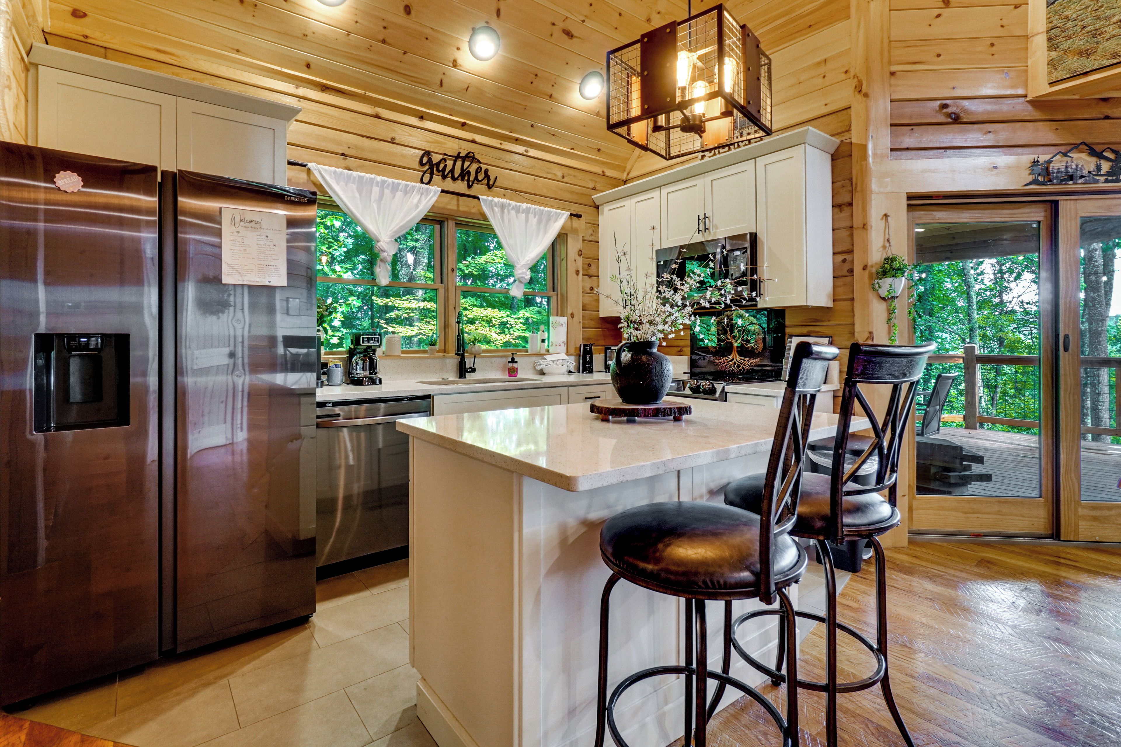 A modern kitchen with stainless steel appliances, a central island with bar stools, and a view of the outdoors through large windows.
