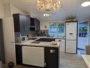 A modern kitchen with a central island, built-in appliances, and a large window providing natural light. - Modern, cosy pet-friendly lodge quiet location. perfect for peaceful getaways. (Milford on Sea)