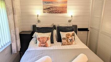 A hotel room with a bed, two pillows with animal prints, a painting above the bed, and a window with curtains.