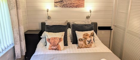 A hotel room with a bed, two pillows with animal prints, a painting above the bed, and a window with curtains.