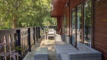 A wooden deck with wicker furniture and a glass door leading to a covered area.