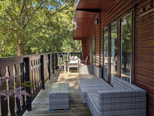 A wooden deck with wicker furniture and a glass door leading to a covered area.