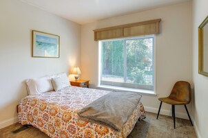 Quarto com cama, cadeira, janela com persianas, mesa de cabeceira com abajur e um quadro na parede.