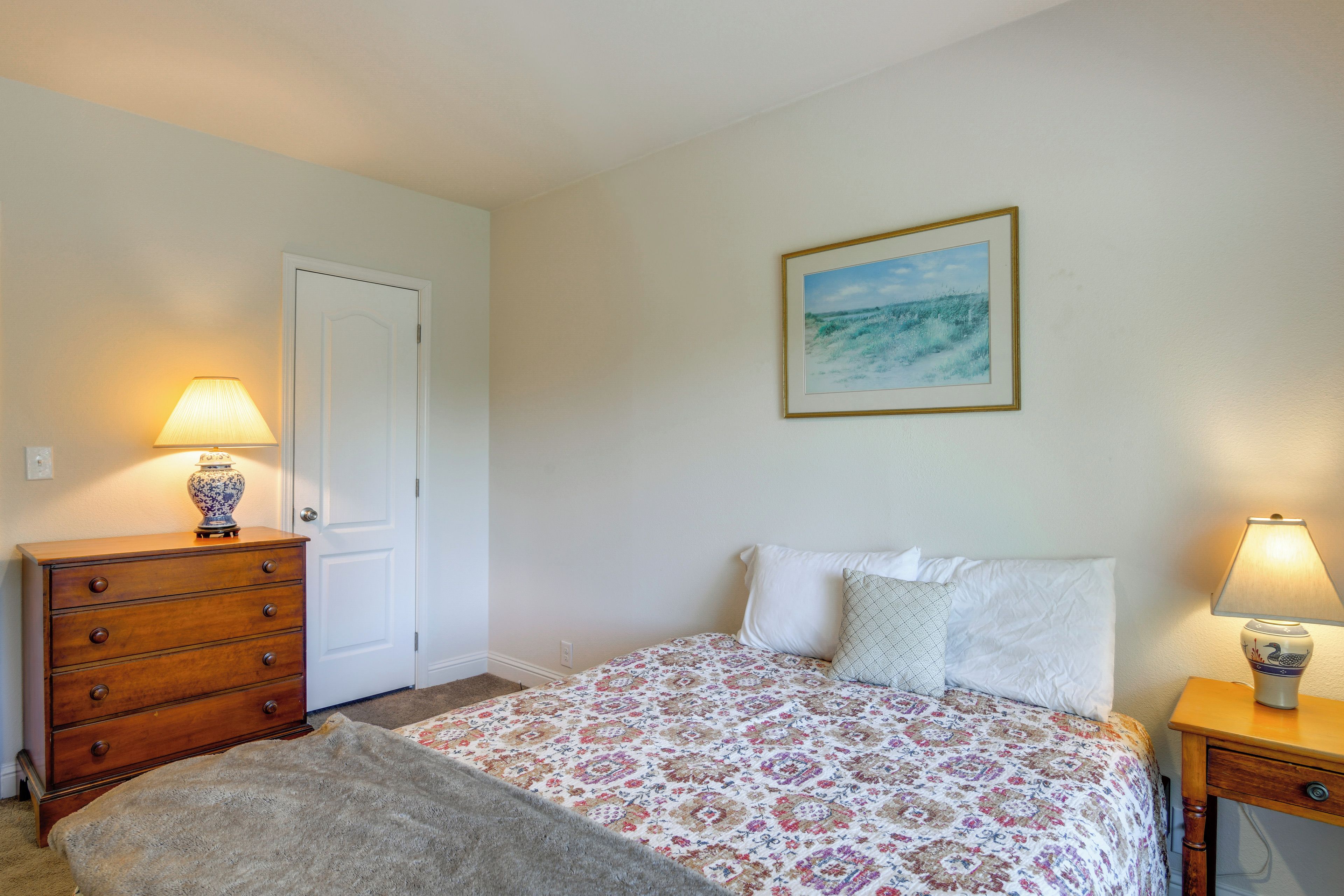 A bedroom with a bed, a dresser, a lamp, and a painting on the wall.