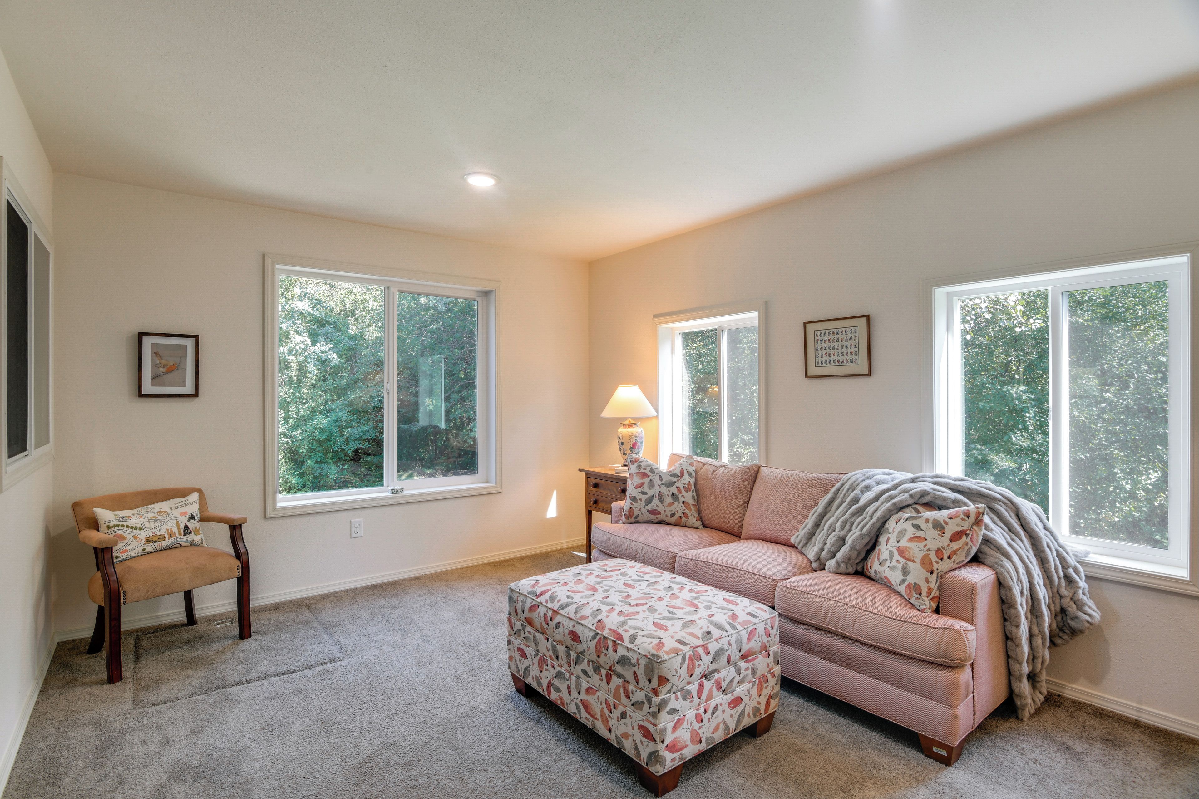 A spacious living room with a large window, a sofa, an ottoman, and a chair.