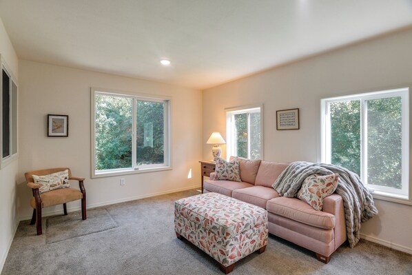A spacious living room with a large window, a sofa, an ottoman, and a chair.