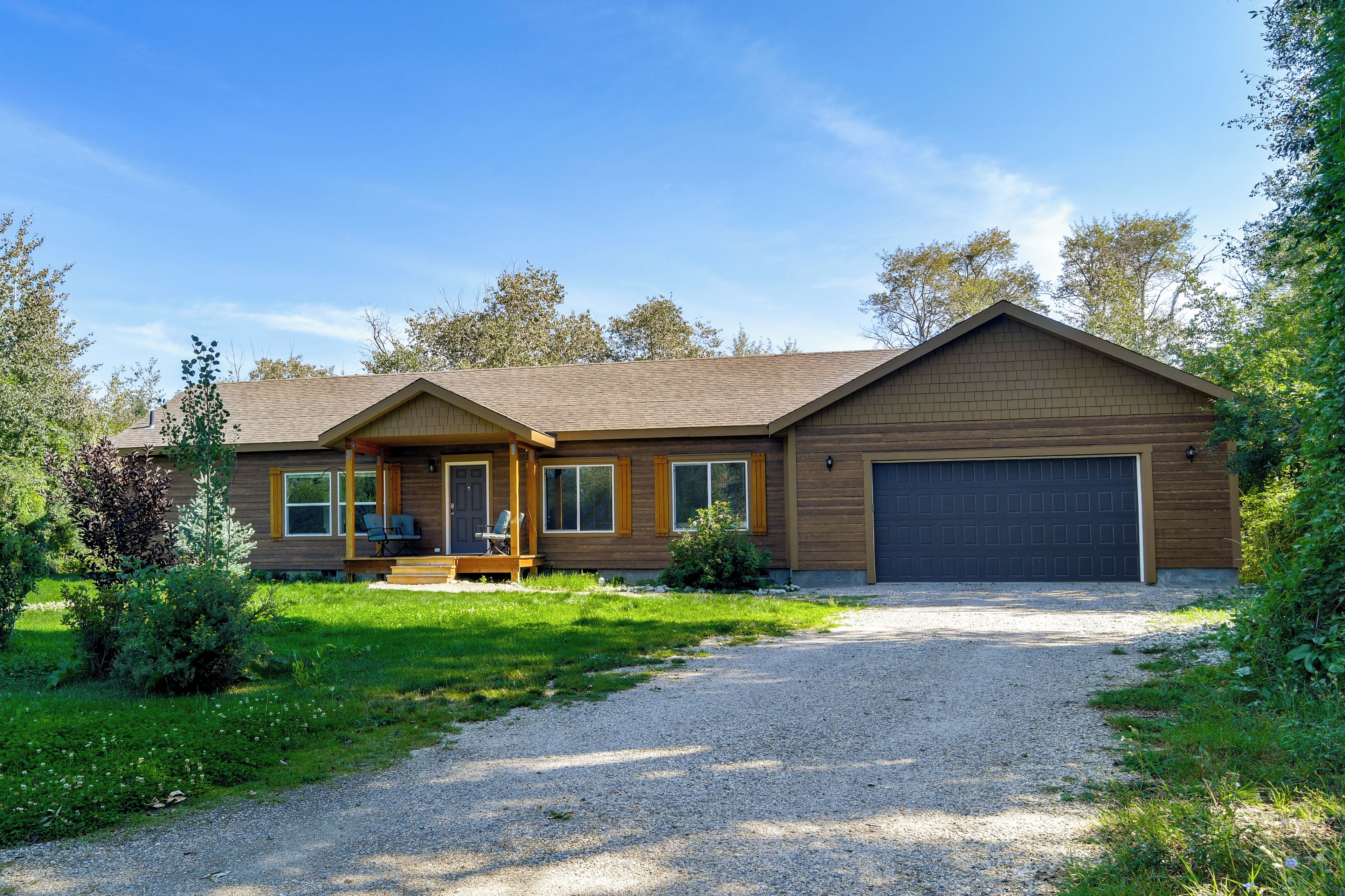 A two-story house with a covered porch, a garage, and a gravel driveway.