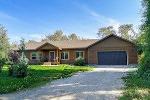 A two-story house with a covered porch, a garage, and a gravel driveway.